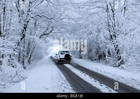 Winterlandschaft Rückansicht Auto fährt auf einer schneebedeckten Landstraße unter spektakulären, schneebedeckten Bäumen in Doddinghurst Essex England Großbritannien Stockfoto