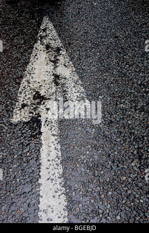 Ein Bild eines Pfeils lackiert in weiß auf nassem Asphalt. Stockfoto
