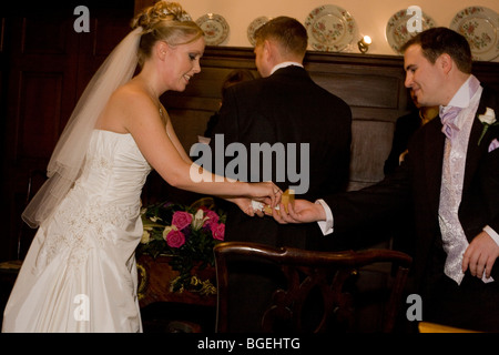 Eine Braut reicht für einen Ring von dem besten Mann hinter ihr bald-zu-sein Mann in einer standesamtlichen Trauung in einer lizenzierten Zeremonie. Stockfoto