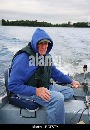 Senior ältere erfahrene Angelführer fahren Alumnacraft Fischerboot im nasskalten Wetters kabbeliges Wasser Gefolge Wellen Aktion Stockfoto