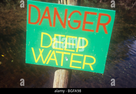 Holzschild auf Mast mit Wasser und Schlamm hinter lackiertem grün mit roten und gelben Schriftzug Gefahr Tiefenwasser Stockfoto