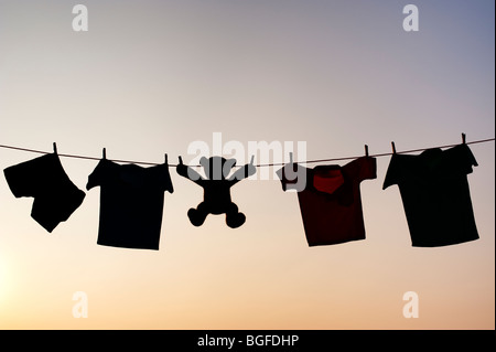 Kleidung der Kinder und Teddybär auf eine Wäscheleine Silhouette in der Dämmerung. Indien Stockfoto