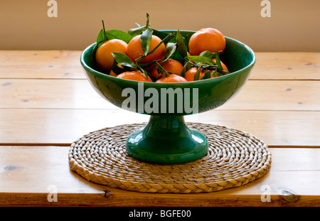 Clementinen mit Blättern in einem grünen Obstschale. Stockfoto