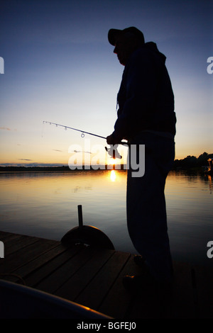 Silhouette Fischer am Bootsdock mit Rute und Rolle in der hand Sonnenuntergang Stockfoto