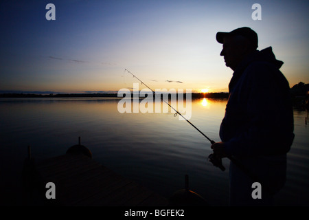 Silhouette Fischer am Bootsdock mit Rute und Rolle in der hand Sonnenuntergang Stockfoto