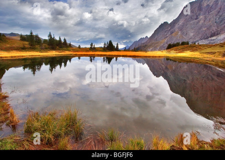 Der glatte Bergsee spiegelt den bewölkten Himmel in den Alpen Stockfoto