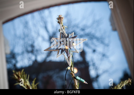 Ein festlicher Stern wird über einen Weihnachtsbaum in einem Erker aus einem Wohnzimmer platziert. Stockfoto