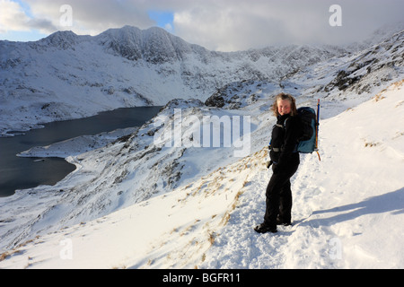 Eine weibliche Hügel Walker auf der Snowdon Pyg Strecke unter winterlichen Bedingungen. Blick über Llyn Llydaw und die Gipfel des Y Lliwedd Stockfoto