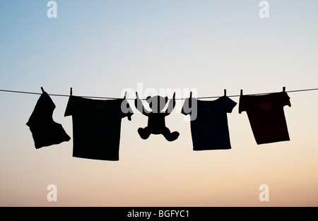 Kleidung der Kinder und Teddybär auf eine Wäscheleine Silhouette in der Morgendämmerung. Indien Stockfoto