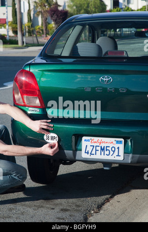 Man platziert eine 38 Meilen pro Gallone Kraftstoff Effizienz Autoaufkleber auf Toyota Echo Auto installiert. Kalifornien, USA Stockfoto