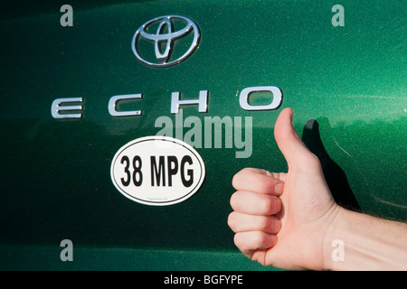 Nahaufnahme einer Person, die Daumen hochhalten, neben 38 Meilen pro Gallone Kraftstoff Effizienz Autoaufkleber auf grün Toyota Echo Auto. Stockfoto