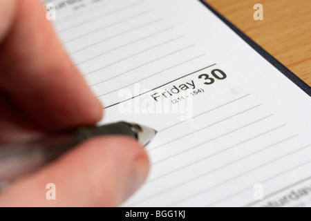 Mans Hand mit Stift schreiben einen Eintrag in einem Schreibtisch Papiertagebuch auf eine leere Freitag Stockfoto