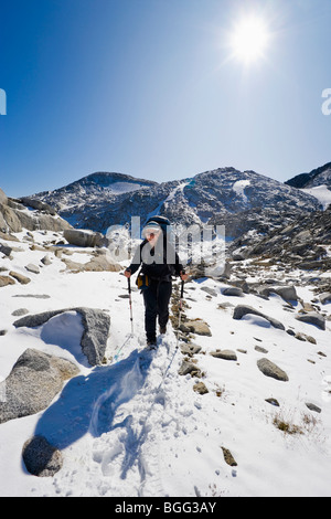 Eine Frau trägt einen Rucksack, Wandern im Schnee durch einige hochalpine Landschaft, Verzauberung Lakes Wilderness Area Stockfoto