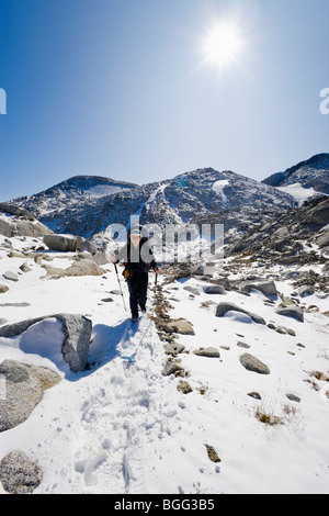 Eine Frau trägt einen Rucksack, Wandern im Schnee durch einige hochalpine Landschaft, Verzauberung Lakes Wilderness Area Stockfoto