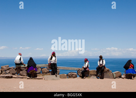 & Männer der Insel Taquile sitzen an Wand in traditioneller Kleidung mit Blick auf Lake Titicaca Stockfoto