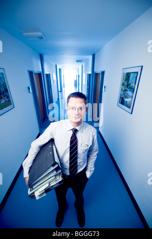 Geschäftsmann in einem Büro Flur stehen, hält Dateien, Vorderansicht Stockfoto