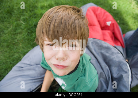 dumme Porträt eines sieben Jahre alten Jungen auf einen Schlafsack im Freien sitzen, warten, dass etwas zu tun, camping. Stockfoto