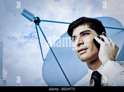 Eine junge männliche Unternehmer auf ein Handy mit Satellitenschüssel im Hintergrund. Stockfoto