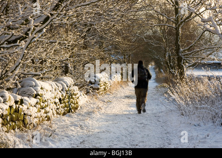 Ein Wanderer auf der verschneiten Fahrbahn, die von Guiseley, die Mauren die Chevin, in der Nähe von Leeds in West Yorkshire führt Stockfoto