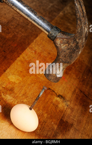 Stock Foto von einem Nagel in ein Ei auf einem Holztisch gehämmert wird. Stockfoto