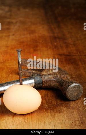 Stock Foto einem rostigen Nagel gehämmert durch ein Ei. Eine alte Hammer liegt neben dem Ei. Stockfoto