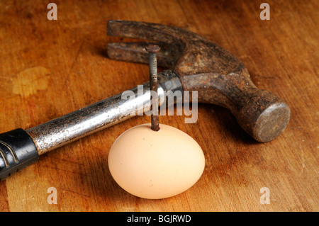 Stock Foto einem rostigen Nagel gehämmert durch ein Ei. Eine alte Hammer liegt neben dem Ei. Stockfoto