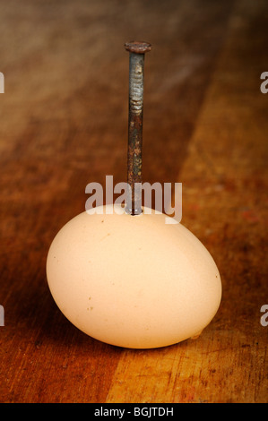 Stock Foto von einem rostigen Nagel gehämmert durch ein Ei in einem Holztisch. Stockfoto