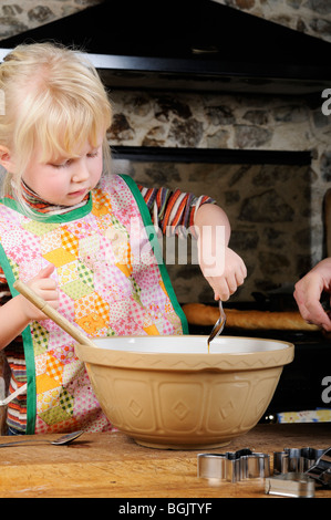 Stock Foto von einem vier Jahre alten Mädchen mit einem Holzlöffel um zu verwechseln einige Cookie-Teig, Kekse zu machen. Stockfoto