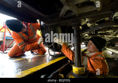 Zwei Mechaniker Montage Schneeketten auf ein Bus-Rad mit einem Bus Garage Inspektion Grube. Stockfoto