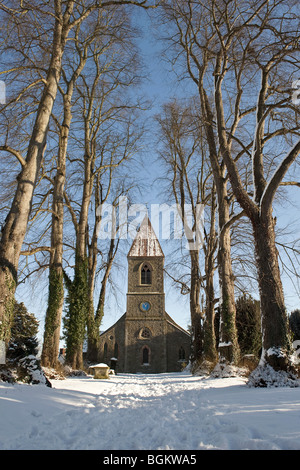 Blick nach unten eine Allee von Bäumen auf dem Schnee bedeckt Steinmauern Dorfkirche und Memorial Friedhof vor blauem Himmel Stockfoto