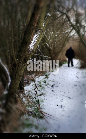 einsamer Mann Walkoing durch Schnee bedeckt Pfad in Holz Stockfoto