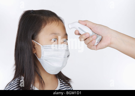 Mädchen tragen Mundschutz und eine Fieber messen auf der Stirn Stockfoto