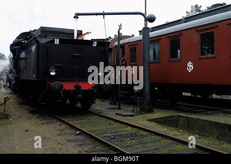 Ein Dampf angetriebene Lokomotive vorbei an alten Wagen am Bahnhof in Brosarp Scania in er südlichen Teil von Schweden. Stockfoto