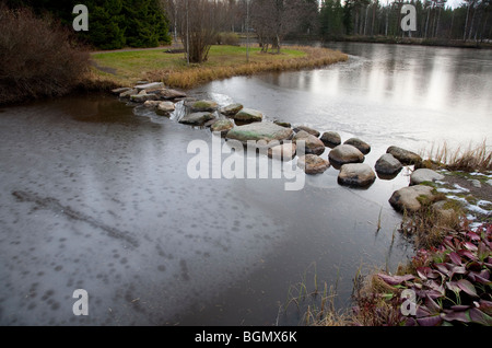 Steine über einen gefrorenen Gartenteich zu treten, Finnland Stockfoto