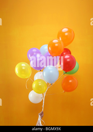 bunte Luftballons in einem Bündel von einer Hand mit orangem Hintergrund statt Stockfoto