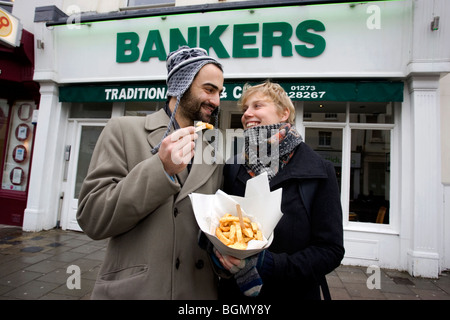 Ein junges Paar genießen Sie einen kleinen Teil der Chips vor Bankern traditionellen Fish &amp; Chips Restaurant und Take-away, Brighton, UK. Stockfoto