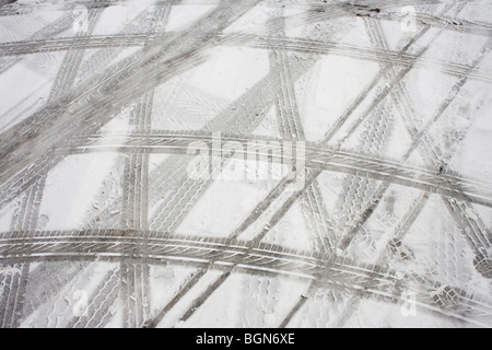 Abstrakt (Reifen) Lauffläche Reifenspuren sind als abstrakte Muster auf Schneeschmelze nach schlechtem Wetter auf einem Supermarkt-Parkplatz links. Stockfoto