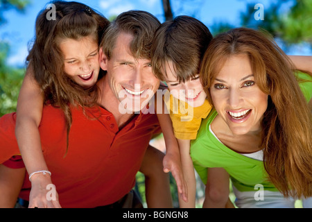 Eine moderne Familie Vater, Mutter, Tochter und Sohn spielen zusammen und haben dabei Huckepack in einem park Stockfoto