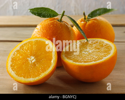 Ganze und geschnittene frische Orangen mit Blättern Stockfoto