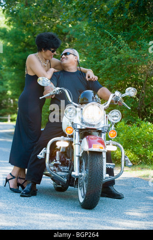 Senior Mann sitzt auf einem Motorrad mit einer reifen Frau, die neben ihm stehenden Stockfoto