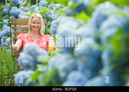Mitte Erwachsene Frau in einem Sessel sitzend und hält eine Flasche Saft Stockfoto