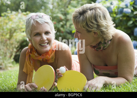 Reife Frau mit ihrer Schwester auf dem Rasen liegen und halten Tischtennisschläger Stockfoto