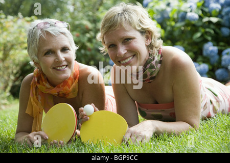 Porträt einer reifen Frau mit ihrer Schwester auf dem Rasen liegen und halten Tischtennisschläger Stockfoto