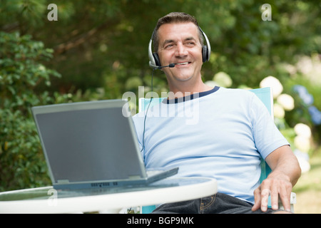 Reifer Mann trägt Kopfhörer und einen Laptop verwenden Stockfoto
