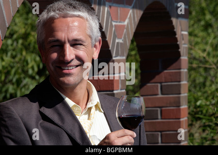 Winzer mit Glas Rot Wein stehen vor der Mauer in seinem Weinberg Stockfoto