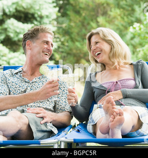 Älteres paar lehnen sich auf Liegestühlen und Toasten mit Cocktail Gläser Stockfoto