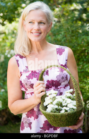 Nahaufnahme einer reifen Frau hält einen Korb mit Blumen Stockfoto