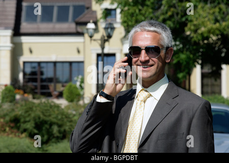 Reife schöne Geschäftsmann steht vor dem Haus mit Handy-Lächeln Stockfoto