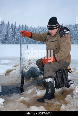 Älterer Mann Check-Fischernetze im Winter, Finnland Stockfoto