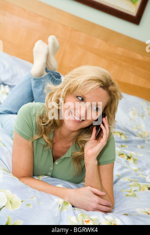 Kaukasischen Frau in den späten 30er Jahren im Bett reden über ein Handy. Stockfoto